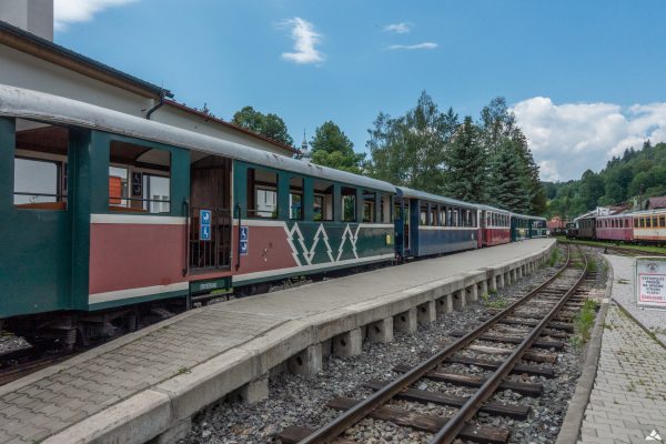 Szereg różnokolorowych wagonów stojących przy betonowym peronie.